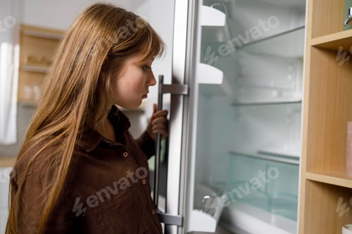 Preview: Young woman looking in empty refrigerator