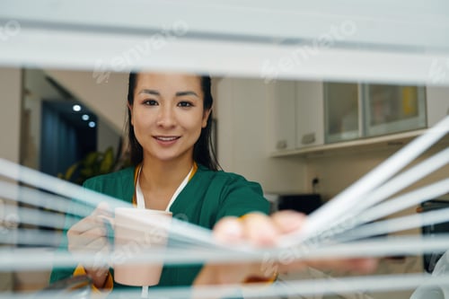 Preview: Portrait of Smiling Woman Peeking Through Window Blinds