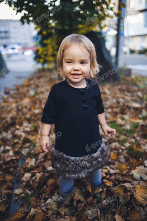 Preview: A little girl of 1.5 years is standing and smiling. The child throws leaves. Cheerful girl in the