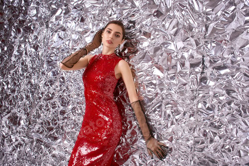 Preview: Festive celebration with a beautiful young woman in sparkling red attire against silver backdrop