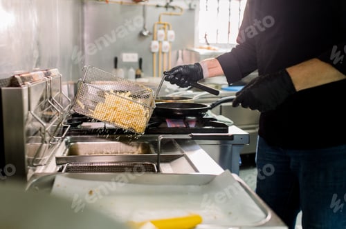 Preview: Crop anonymous male chef in black gloves with deep fryer pan preparing French fries in kitchen of re