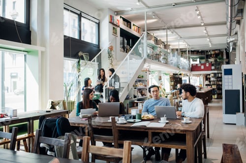 Preview: Young businesswomen and businessmen remote working having meeting at cafe table