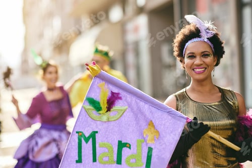 Preview: Happy African American woman holding Mardi Gras flag during the carnival.