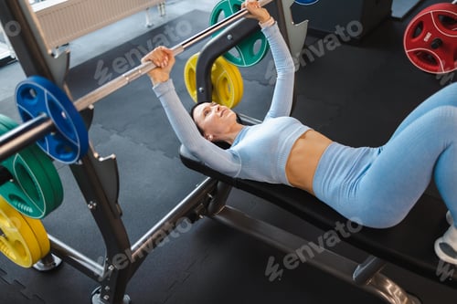 Preview: Fitness woman lifting barbell while lying on bench