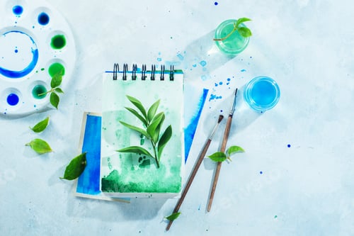 Preview: Artist workplace with tools and plants, green and blue watercolor sketchbooks, brushes and color
