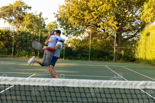 Preview: Happy caucasian couple playing tennis embracing on outdoor tennis court