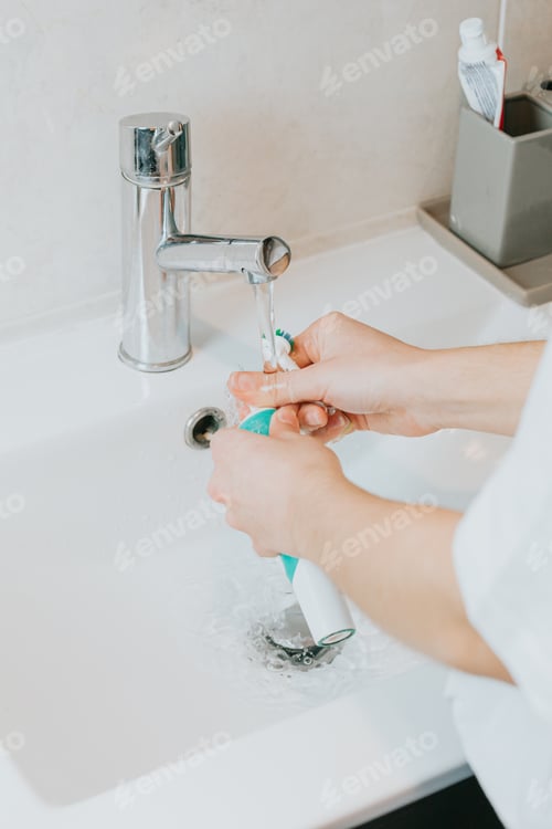 Preview: A woman washing his electrical toothbrush pieces with water after brushing his teeth