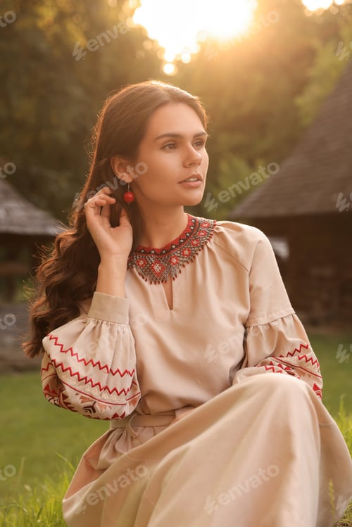 Preview: Beautiful woman wearing embroidered dress in village on sunny day. Ukrainian national clothes