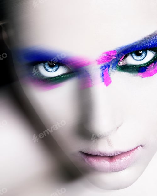 Preview: Close-up portrait of a woman with striking blue eyes and vibrant pink and blue makeup.