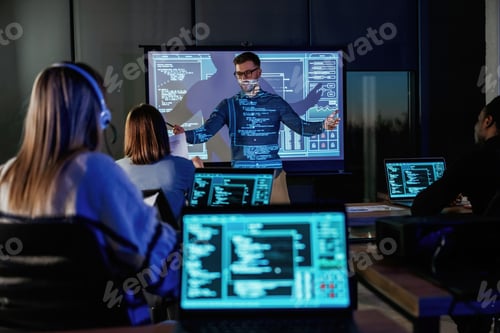 Preview: Audience is with laptops. Male business trainer is against projector with data, teaching people