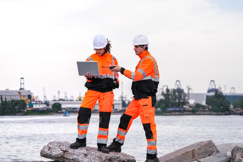 Preview: Two engineers wearing safety uniforms and hard hats communicate using a radio while reviewing data