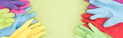 Preview: panoramic shot of multicolored rubber gloves on green background with copy space