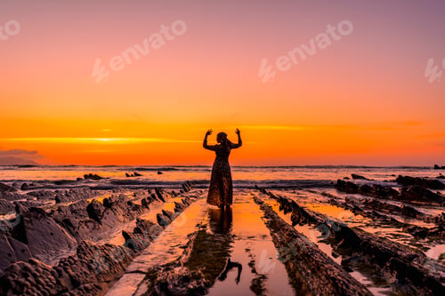 Preview: Young girl with open arms in the water by the rocks