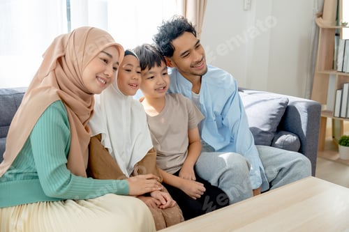 Vista previa: Familia musulmana asiática compuesta por una joven madre, padre, hija e hijo que se abrazan y permanecen juntos en el sofá