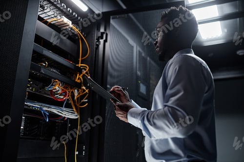 Preview: Backlit black man working with server cabinet and taking notes on clipboard