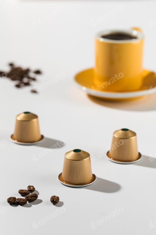 Preview: Coffee capsules with a cup and saucer in the background