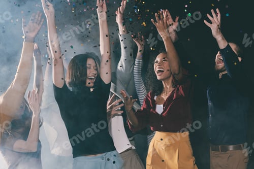 Preview: Group of happy young people dancing and throwing confetti while having fun in night club together
