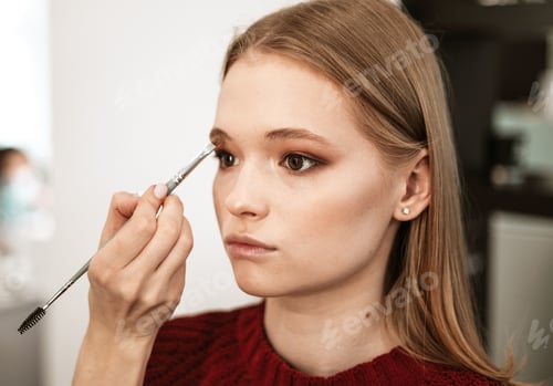 Preview: makeup artist applies eyebrow shadow on a beautiful young woman blonde model, face make up concept,
