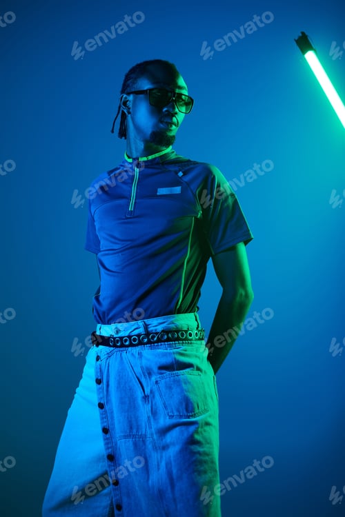 Preview: Young man in stylish attire poses confidently in neon-lit studio at night