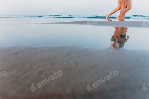 Preview: Two friends walking at sunset on a beach, reflecting in the puddles of sand.