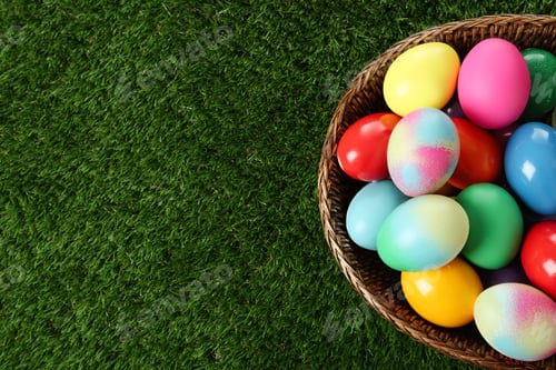 Preview: Wicker basket with bright painted Easter eggs on green grass, top view. Space for text
