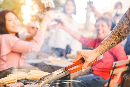 Preview: Tattooed senior man grilling hamburgers for his family at barbecue dinner party