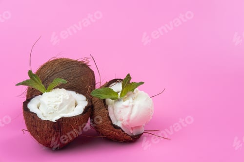 Preview: Vanilla ice cream balls in fresh coconut halves decorated with mint leaves on a pink background