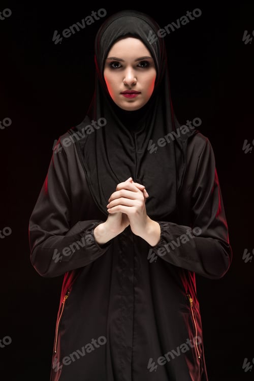 Preview: Portrait of beautiful serious young muslim woman wearing black hijab with hand on hand as praying