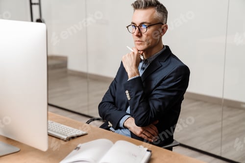 Preview: Focused grey man working with computer while sitting at table in office