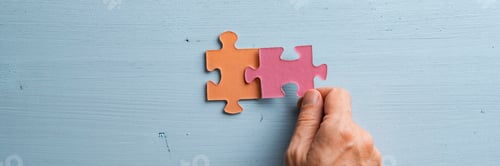 Preview: Wide view image of male hand joining two matching colorful puzzle pieces