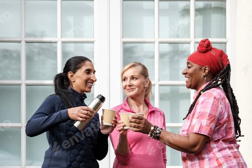 Preview: Multiracial mature women friends sharing coffee outdoors.