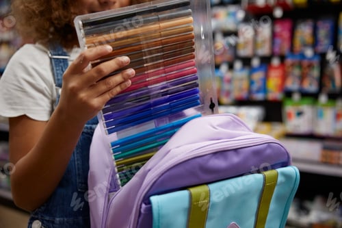 Preview: Girl student choosing colorful markers while shopping at stationery store