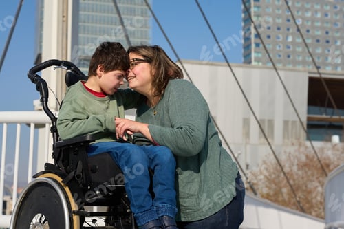Preview: Mother showing affection to son with cerebral palsy in wheelchair on bridge