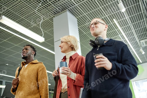 Preview: Multiethnic Young Adults Standing Together Holding Coffee Cups in Office