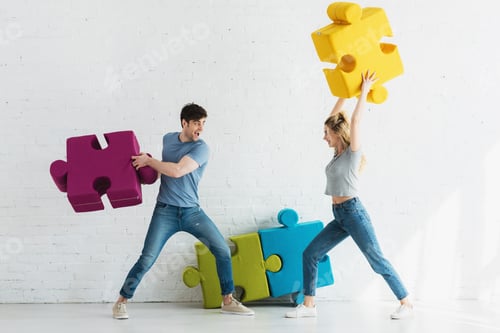 Preview: cheerful woman and happy man fighting with puzzle pieces at home