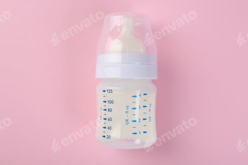 Preview: Feeding bottle with milk on pink background, top view