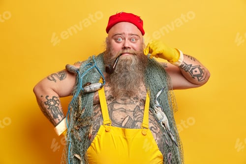 Preview: Funny male sailor curls mustache has smoking pipe in mouth wears red hat overalls and gloves poses a
