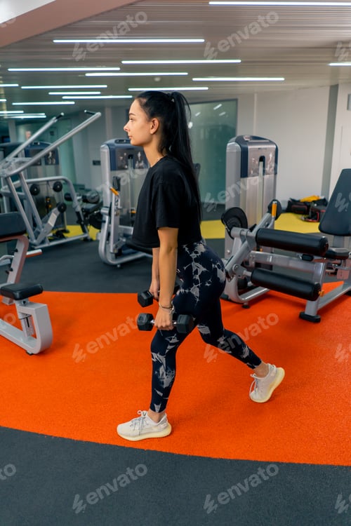 Preview: young girl in sportswear in the gym doing exercises with dumbbells training a healthy lifestyle