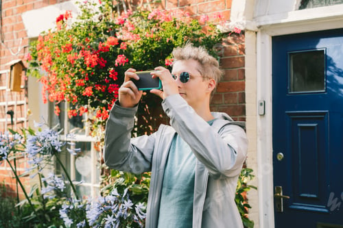 Preview: Young man filming video or taking photo pictures on mobile phone during walking in residential area