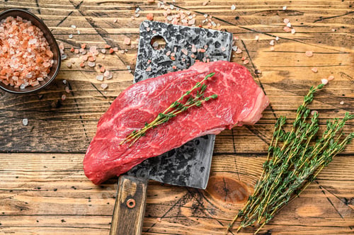 Preview: Raw Striploin steak on a meat cleaver, marbled beef. Wooden background. Top view