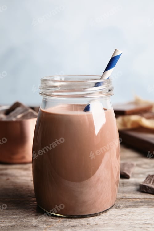 Preview: Jar with tasty chocolate milk on wooden table. Dairy drink