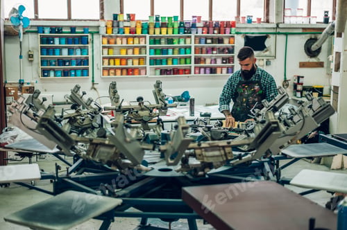 Preview: Male worker pressing ink on frame while using the printing machine in a workshop