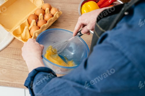 Preview: Top view of unrecognizable man in blue long-sleeve shirt beating eggs in blue plastic bowl