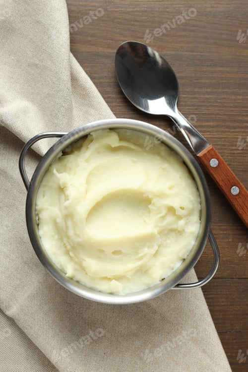 Preview: Mashed potatoes in pan on towel and spoon on wooden background, top view