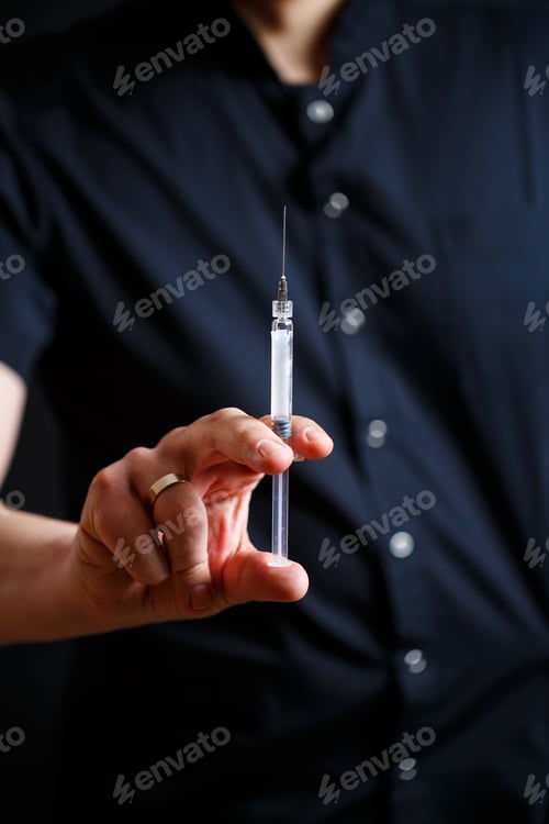 Preview: Male doctor chief physician in a black surgical suit. Close-up portrait. Holds a syringe