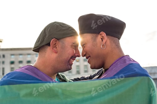 Preview: Gay couple under LGBT rainbow flag while laughing and looking at each other. Concept of Pride. Pride