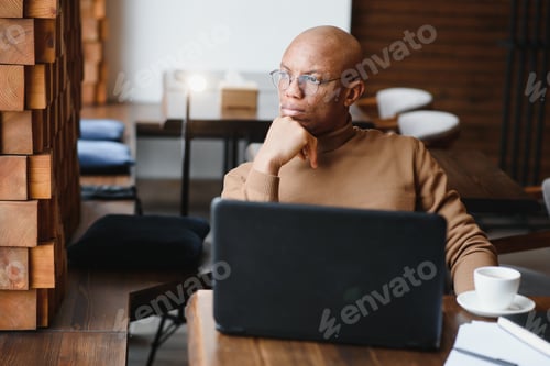 Preview: African-Ameican entrepreneur wearing shirt with rolled up sleeves looking through window
