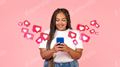 Preview: Cheerful young african american female with pigtails has romantic chat with hearts on smartphone