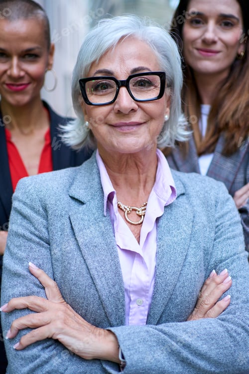 Preview: Portrait empowered female business in suits looking smiling at camera with arms crossed outdoor.