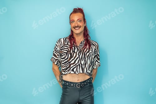 Preview: Non-binary person with red hair and mustache smiling on blue background